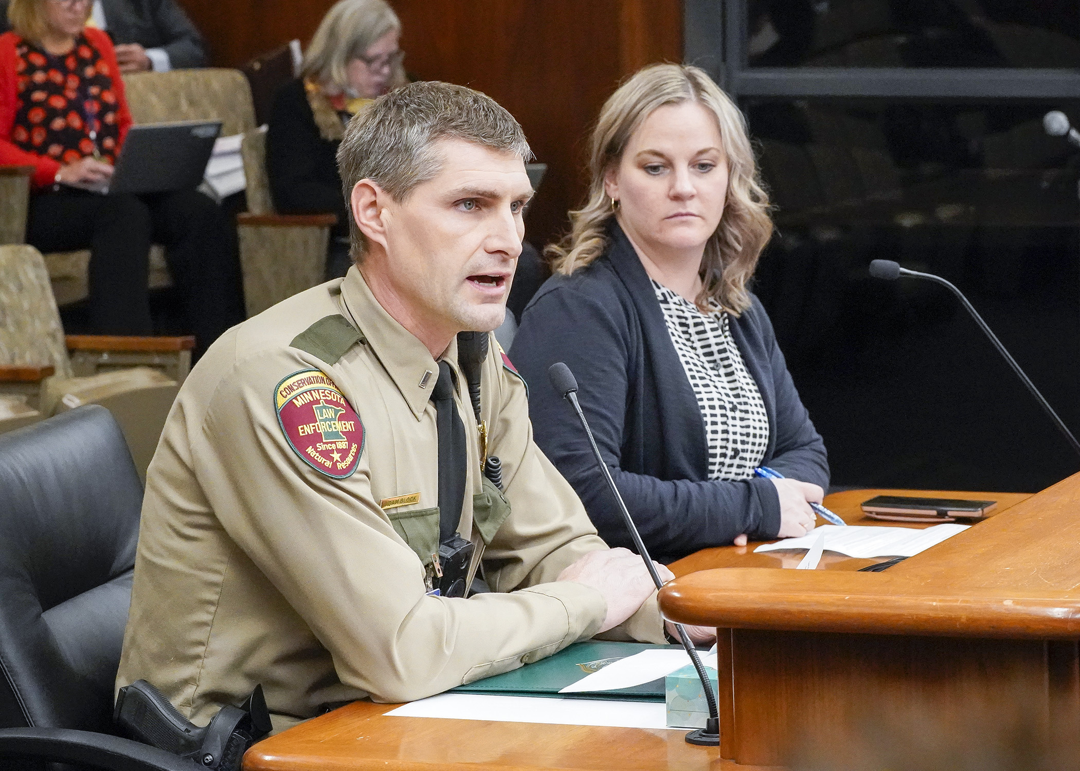 DNR conservation officer Adam Block testifies before the House Environment and Natural Resources Finance and Policy Committee March 1 in support of HF949 sponsored by Rep. Erin Koegel, right. (Photo by Andrew VonBank)